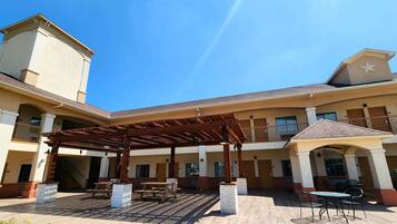 Pátio de hotel com área de estar coberta, mesas ao ar livre e uma fonte central.