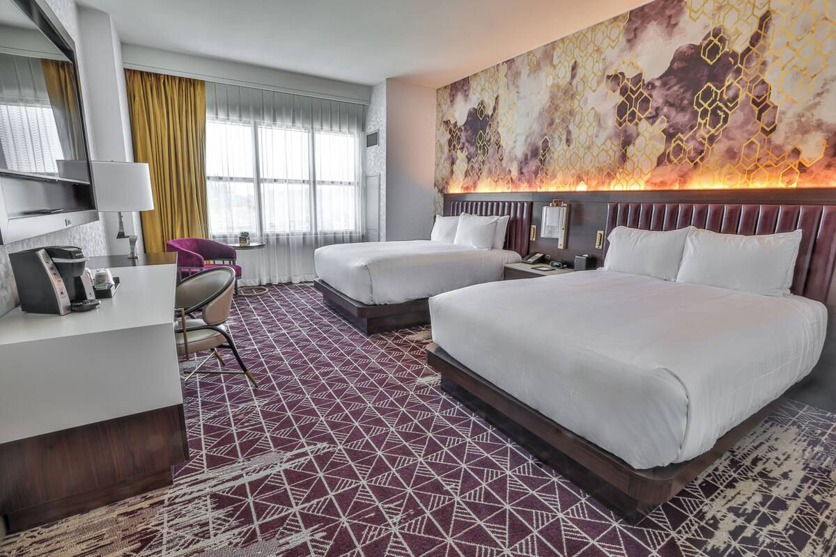 Habitación de hotel con dos camas, un escritorio, una silla y un cuadro abstracto grande en la pared.