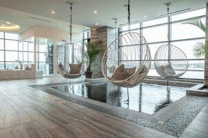 Área de piscina interior moderna con sillas colgantes y suelo de piedra.