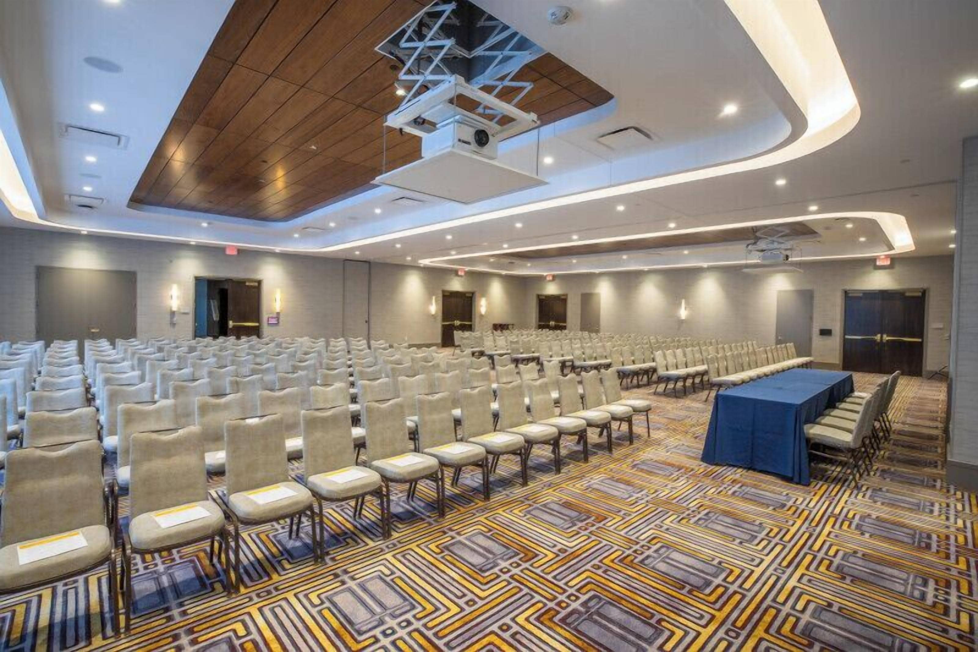 A conference room with rows of chairs, a stage with a blue table, and a patterned carpet.