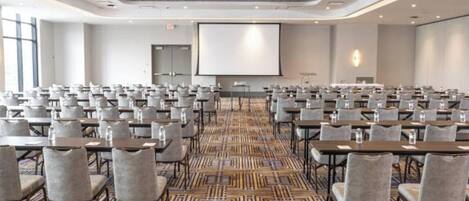 A conference room with rows of tables and chairs, a projector screen, and a patterned carpet.
