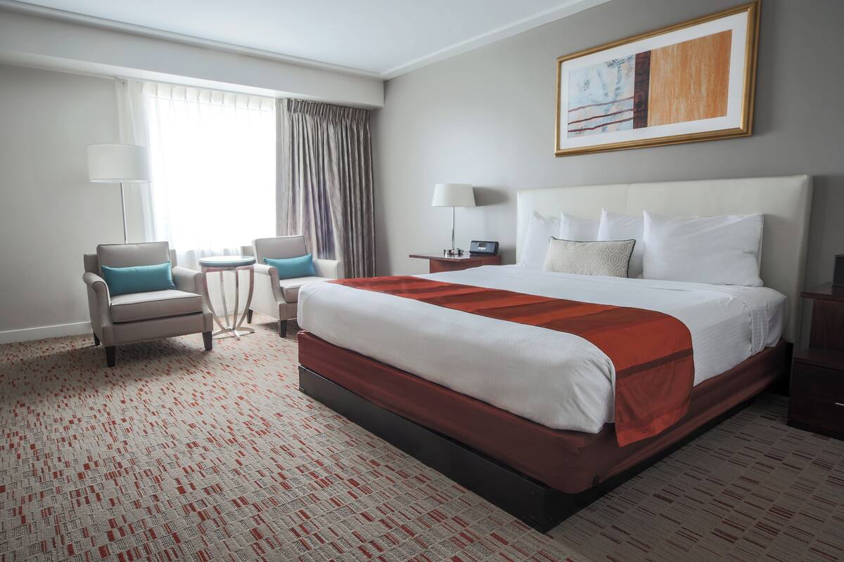 Una habitación de hotel con una cama grande, dos sillones, una mesita, una lámpara y un cuadro en la pared.
