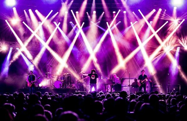 A concert stage with musicians performing, illuminated by stage lights.