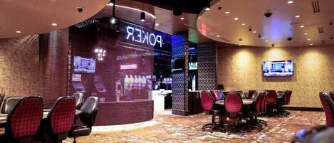A hotel lobby with a poker table area, a reception desk, and a television screen.