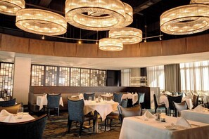 Een restaurant met ronde kroonluchters, gedekte tafels en een uitzicht door een raam met patroon.