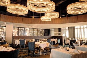 Un restaurante con candelabros redondos, mesas dispuestas para comer y vistas a través de un ventanal decorativo.