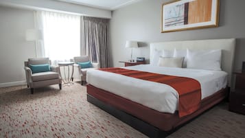 A hotel room with a large bed, two armchairs, a small table, a lamp, and a painting on the wall.
