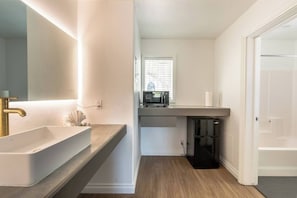 A modern bathroom with a large sink, a mirror, a microwave, and a toilet.