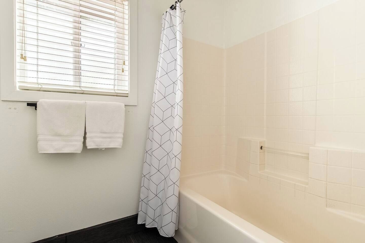 Une salle de bain avec une douche, une fenêtre avec des stores et deux serviettes accrochées au mur.