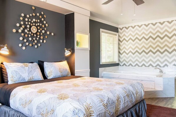 A modern bedroom with a large bed, a wall-mounted light fixture, a window with blinds, and a chevron-patterned wall.