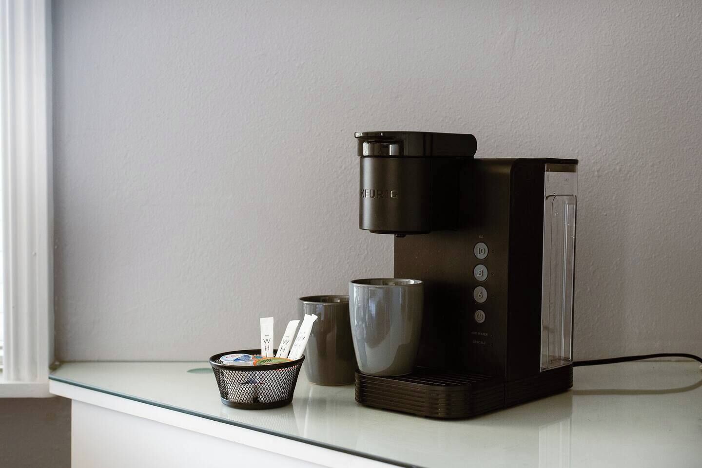 Eine moderne Kaffeemaschine mit Wasserbehälter, Kanne und Tropfschale auf einer weißen Arbeitsplatte.