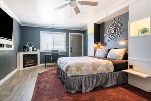 A bedroom with a bed, a desk, a chair, a fireplace, and a ceiling fan.