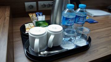 Una bandeja con dos tazas blancas, dos botellas de agua Nestle PureLife, una tetera y algunos paquetes de comida sobre una mesa de madera.