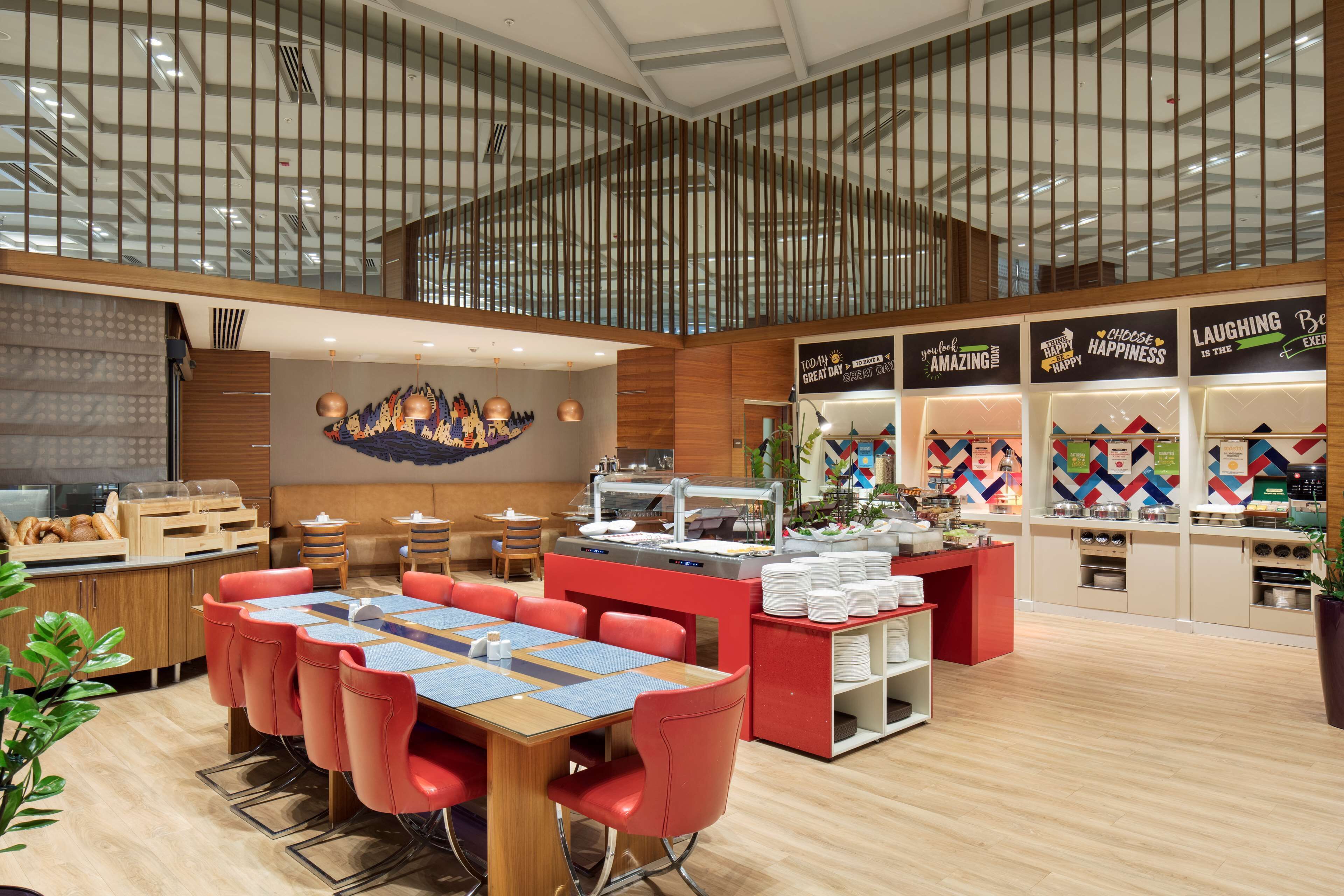 Un restaurante moderno con techo alto, detalles de madera y un área central de comedor con sillas rojas y una mesa de madera.
