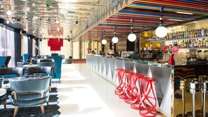 A bar area with a long counter, multiple stools, and a variety of bottles on shelves. - Scandic Paasi (Helsinki)
