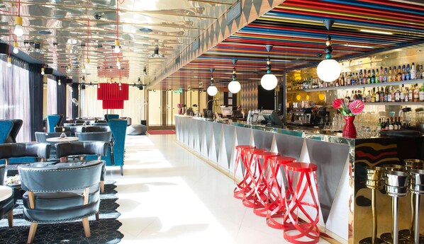 Una zona de bar con una barra alargada, varios taburetes y una selección de botellas en estanterías.
