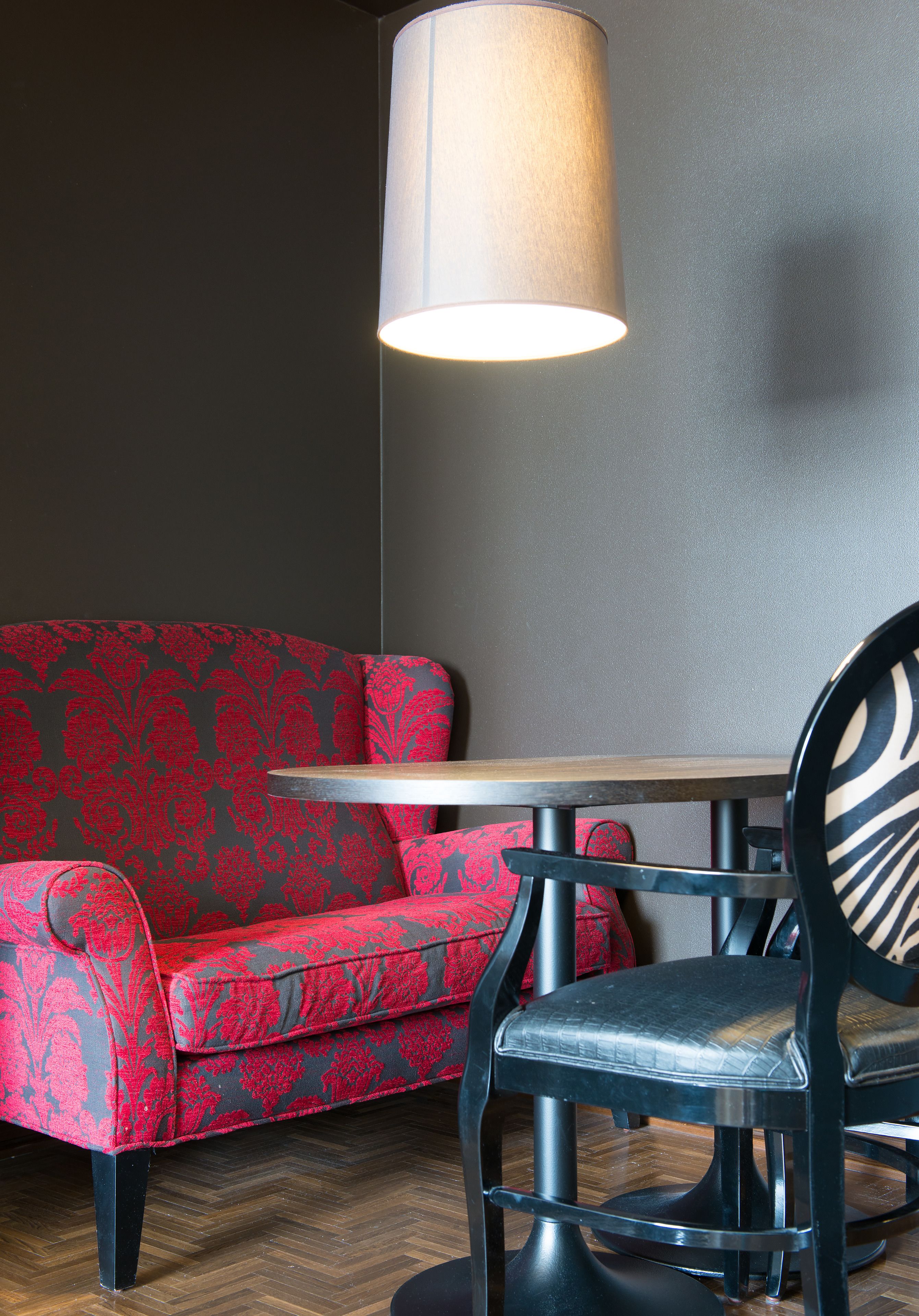 Una habitación con un sofá rojo estampado, una mesa redonda y una silla negra.
