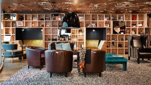 A modern lounge area with leather sofas, a patterned carpet, and a wooden bookshelf filled with various items. - Scandic Paasi (Helsinki)