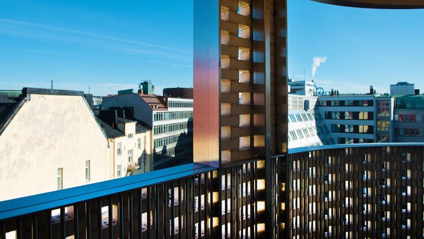 A balcony with a view of a cityscape, including buildings and a smokestack. - Scandic Paasi (Helsinki)