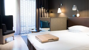 A hotel room with a bed, a desk, a chair, a small table, and a window with curtains. - Scandic Paasi (Helsinki)
