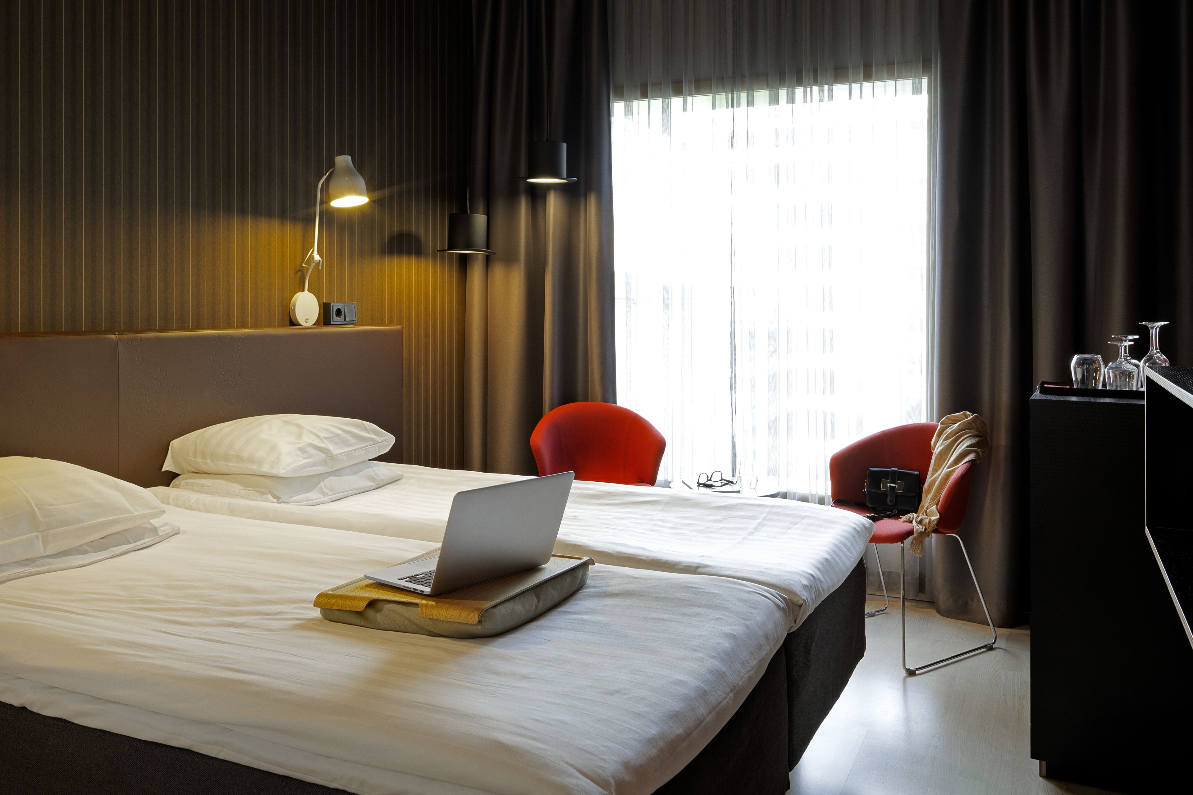 Een hotelkamer met een bed, een laptop, een stoel en een bureau met een lamp.