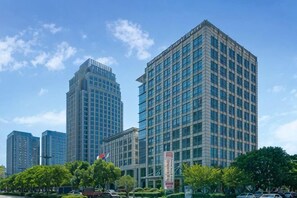 A modern high-rise building with a grid of windows, surrounded by trees and other buildings. - Harbour Oriental Hotel（Beilun Changjiang Road Store） (Ningbo)
