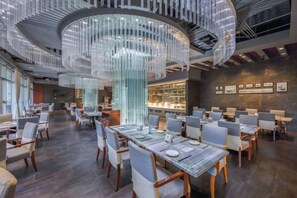 Interior moderno de restaurante con mesas dispuestas para comer, zona de bar y un elemento decorativo en el techo.