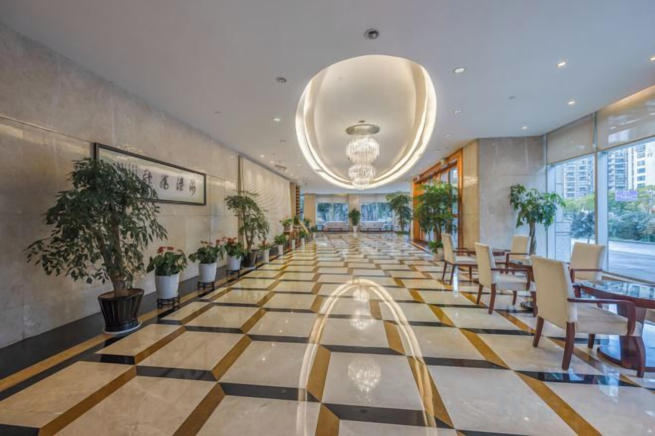 A hotel lobby with a checkered floor, potted plants, and a chandelier.