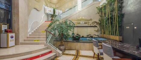 Un vestíbulo de hotel con una recepción, una escalera y una zona de piscina.