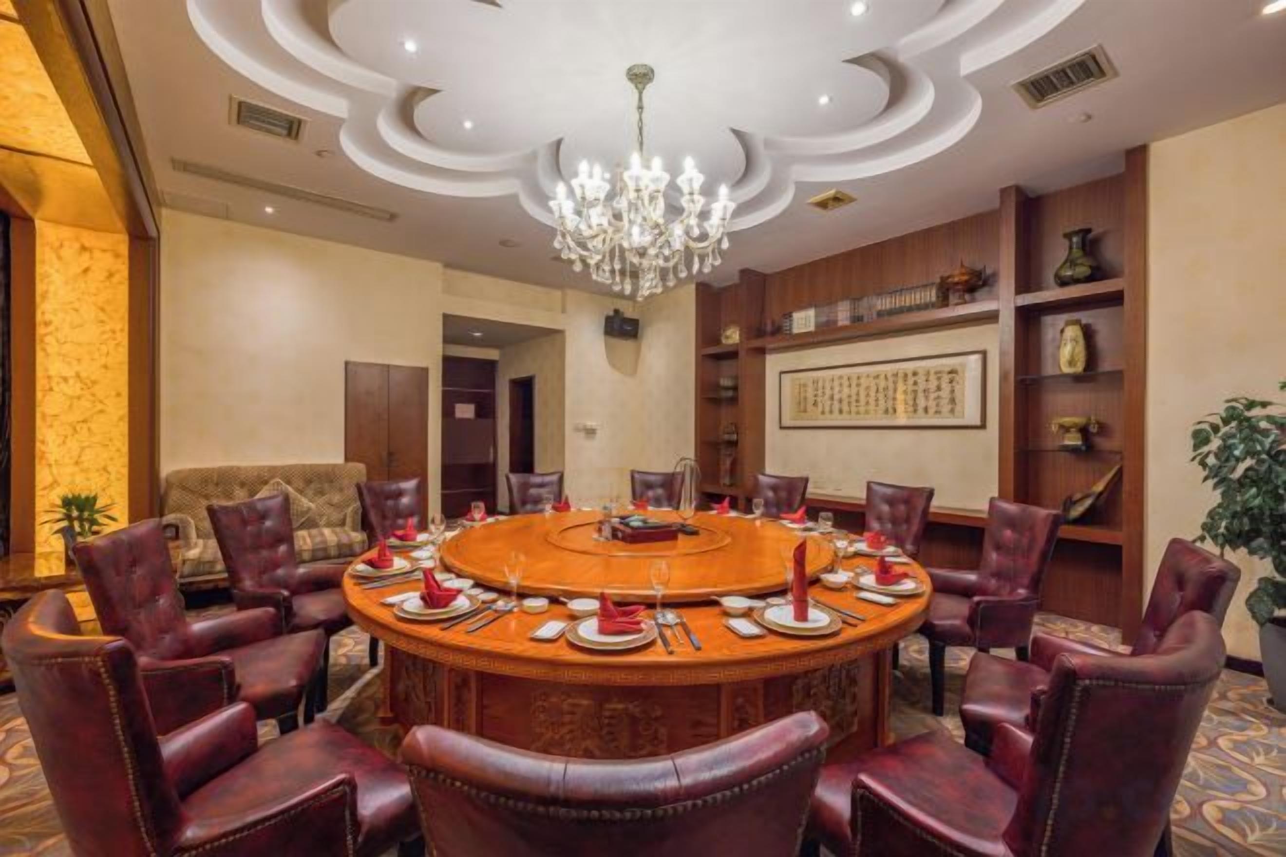 A conference room with a round table, leather chairs, a chandelier, and traditional decor.