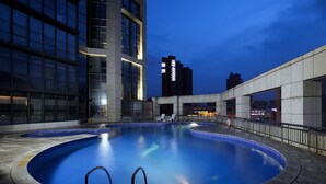 Una piscina interior con agua cristalina, rodeada por un edificio moderno con grandes ventanales y una zona de piscina con sillones de relax.