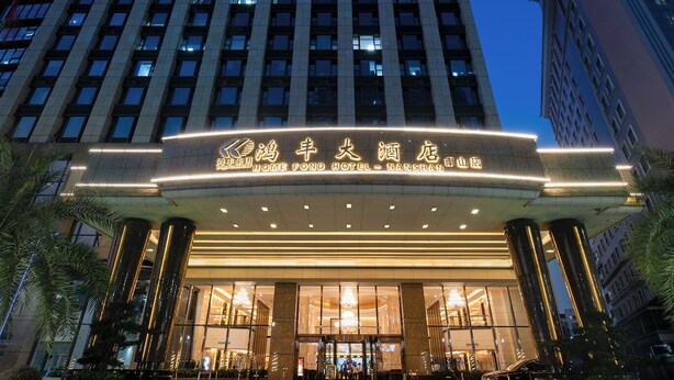 Un hotel con fachada moderna, una entrada destacada y una fuente ornamental al frente.