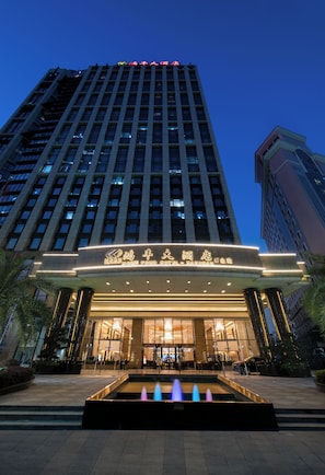 Un hotel con fachada moderna, una entrada destacada y una fuente ornamental al frente.