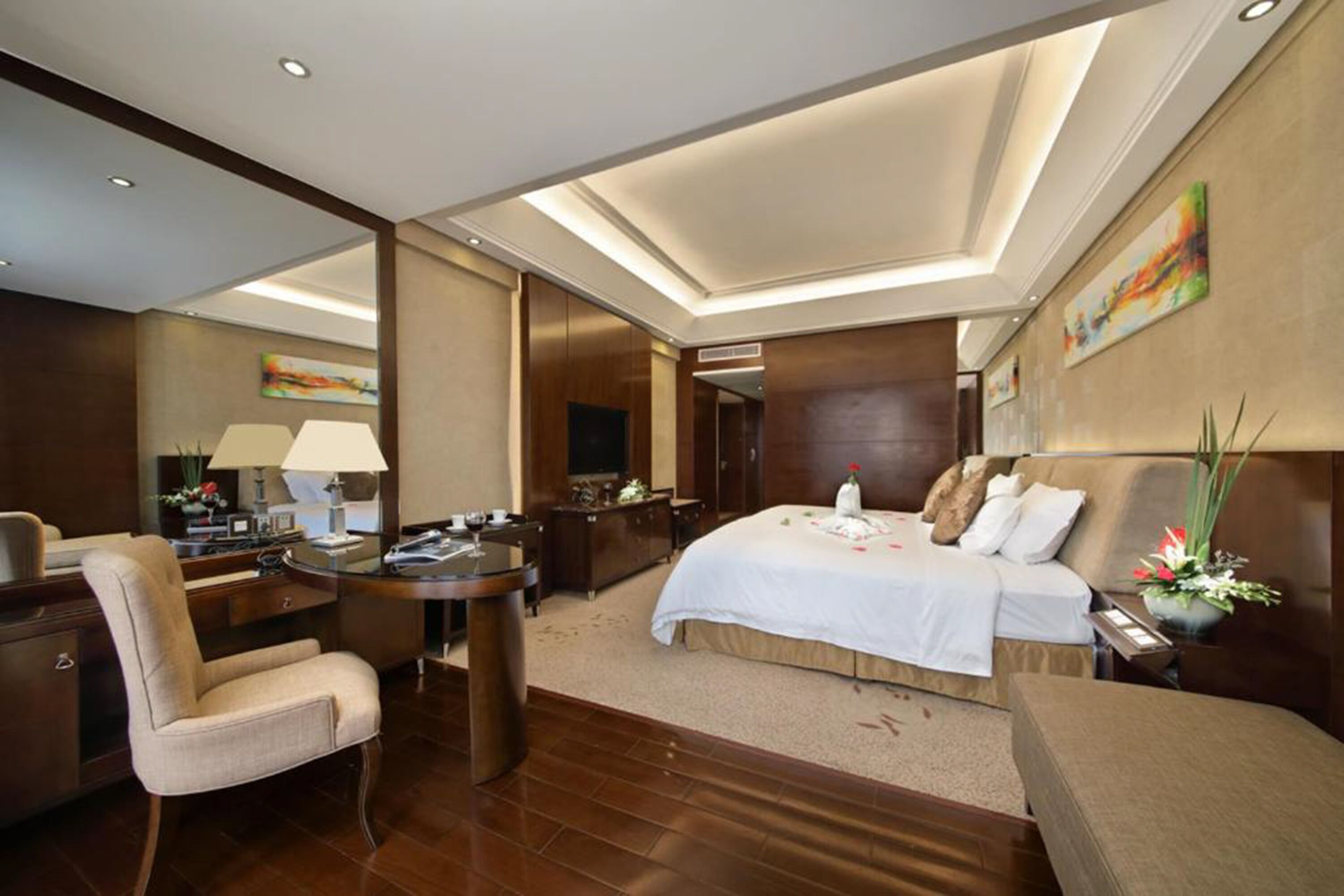 A hotel room with a large bed, a desk with a lamp, a chair, and a small table.