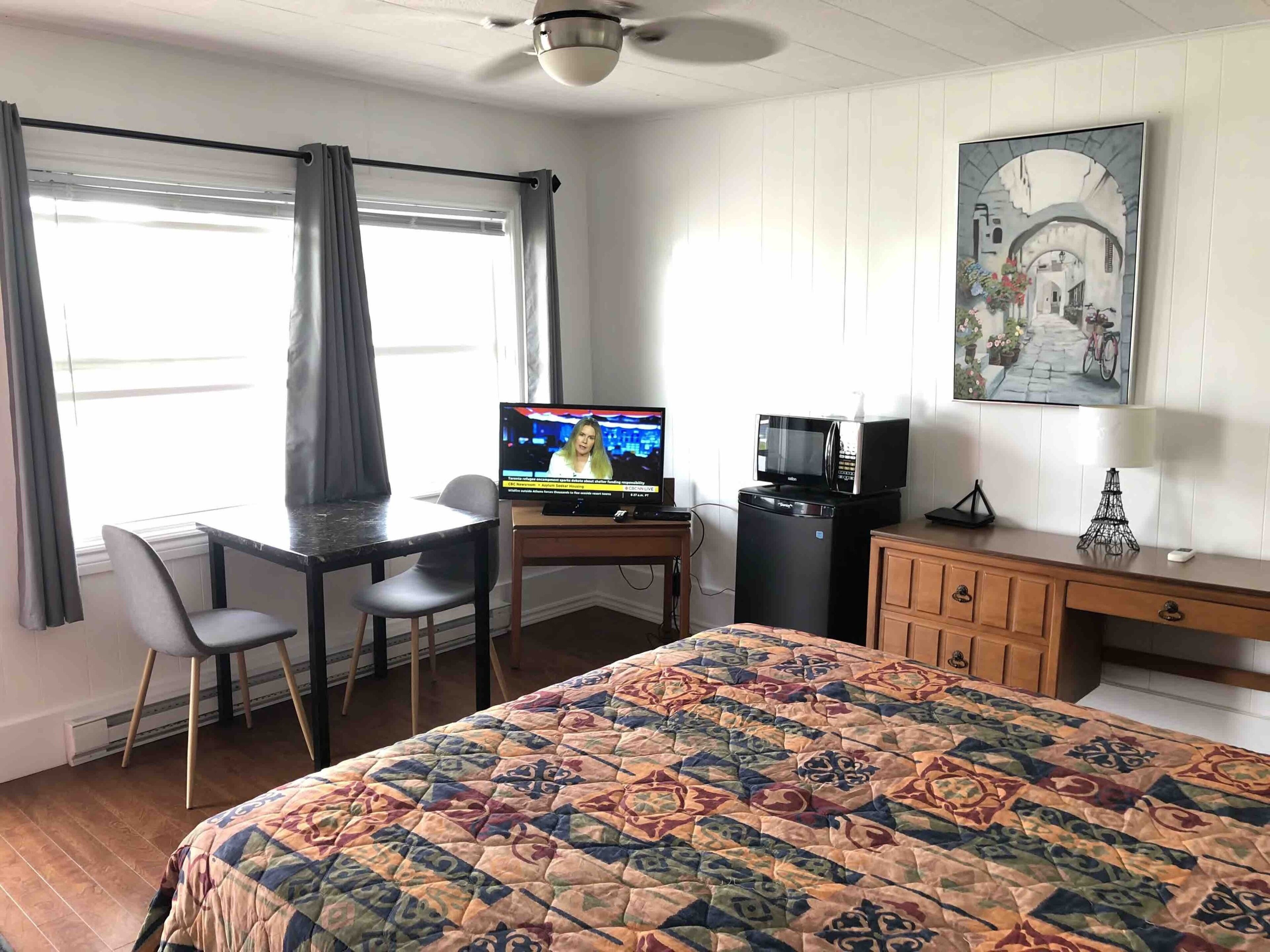 Una habitación de hotel con cama, escritorio, televisor, microondas y un armario.
