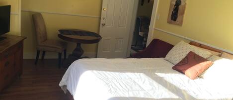 Un dormitorio con una cama, una silla, una mesita y un televisor.