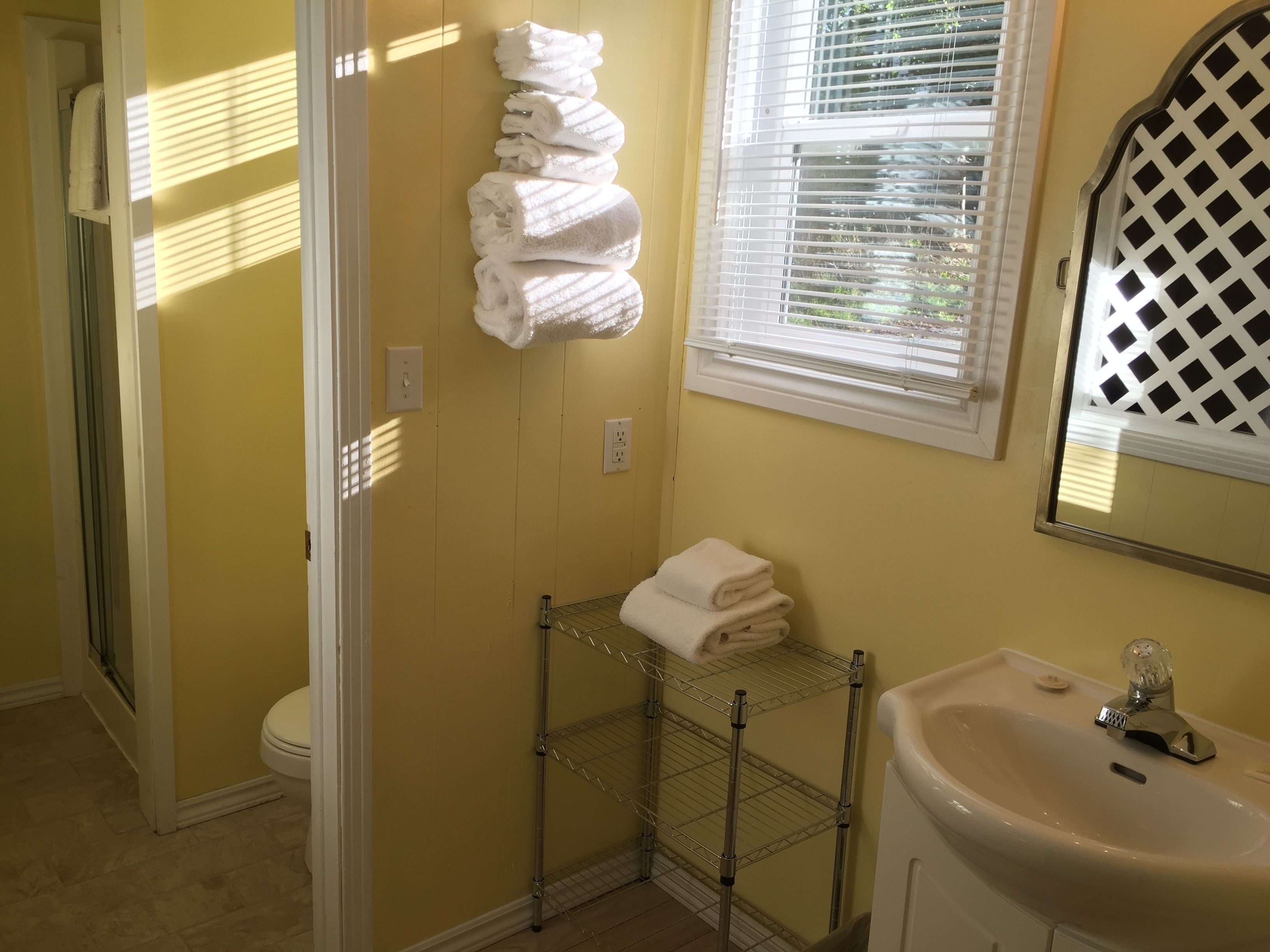A bathroom with a yellow wall, a white sink, a mirror with a lattice design, and a towel rack with folded towels.