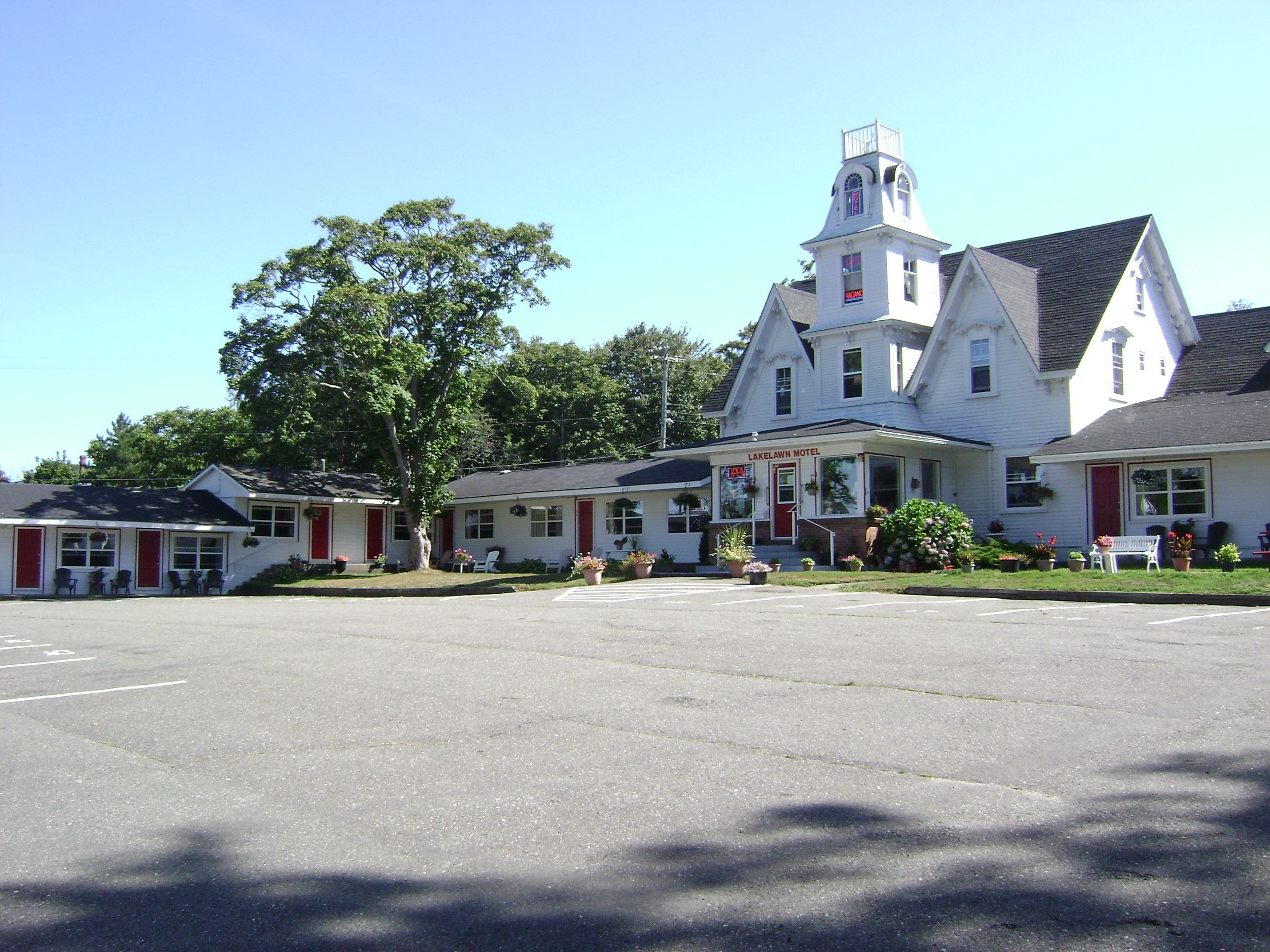 A two-story motel with a prominent tower, a parking lot, and a large tree in front.