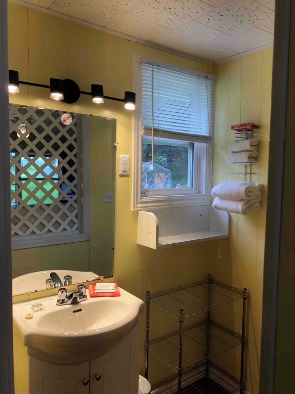 Un baño con lavamanos, espejo, ventana y perchero para toallas.