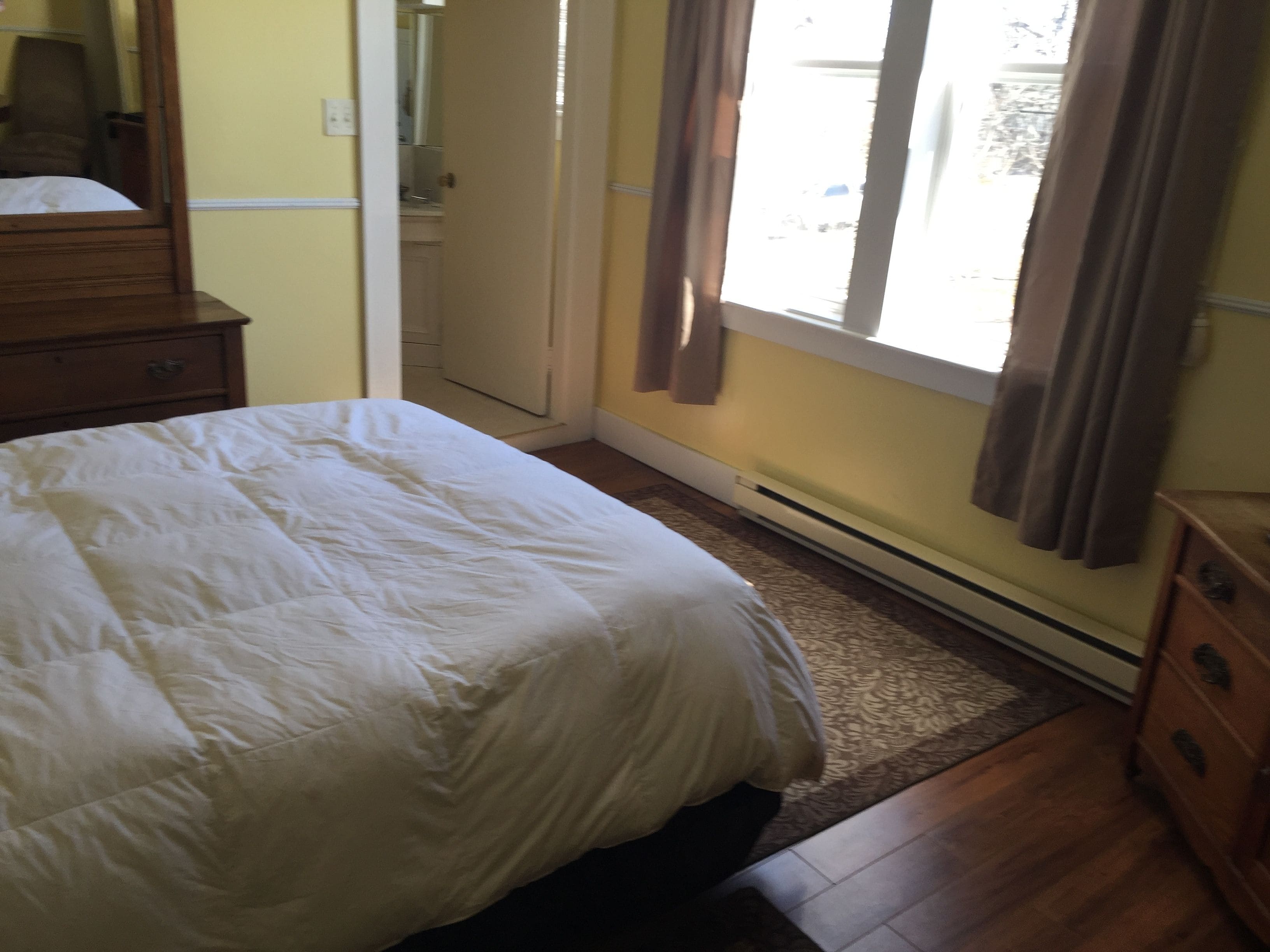 A bedroom with a bed, a dresser, a radiator, and a window with curtains.