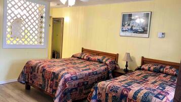 A room with two beds, a ceiling fan, a window with a lattice design, and a framed picture on the wall.