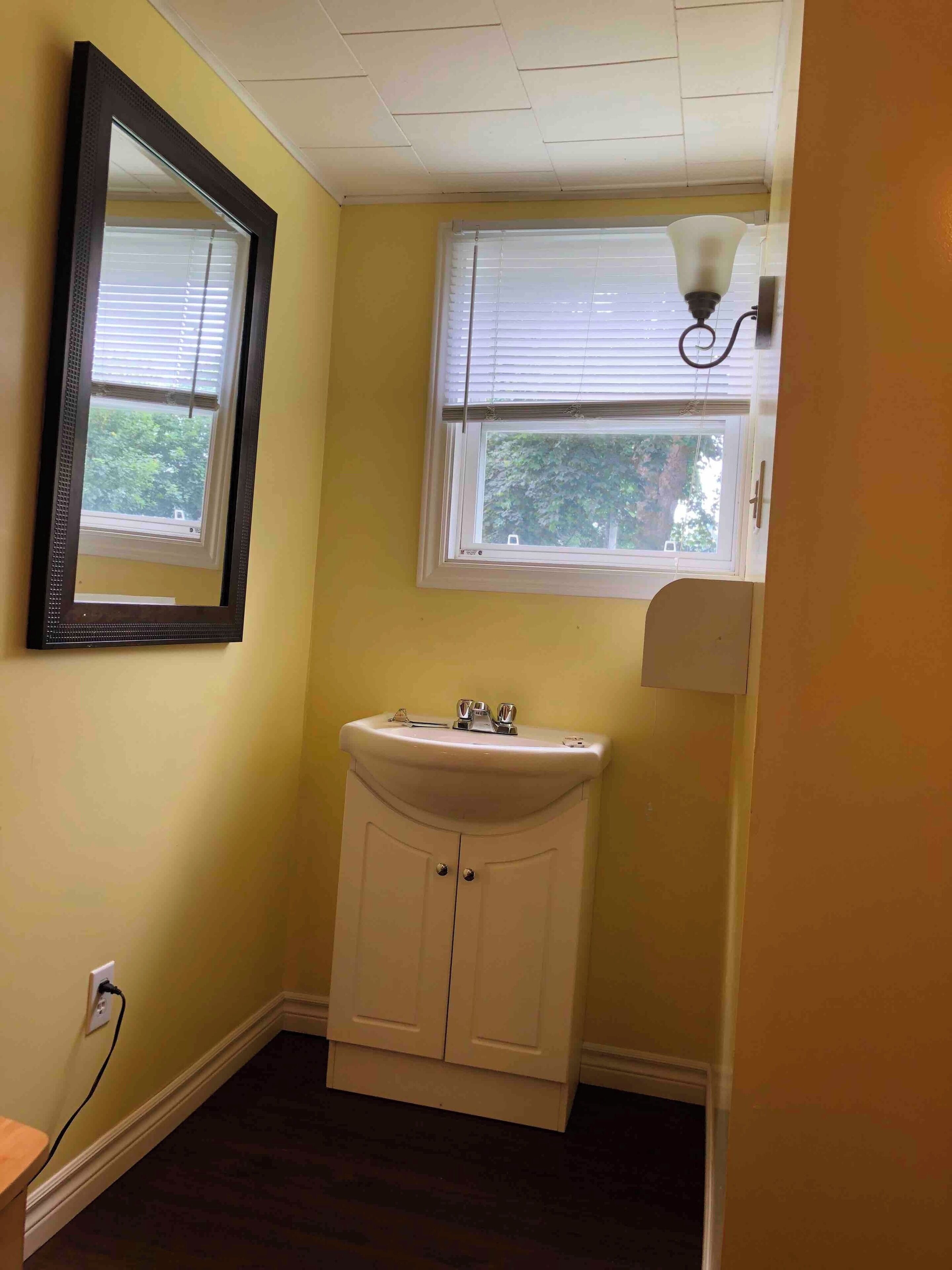 Un baño pequeño con un lavabo blanco, un espejo y una ventana con persianas.