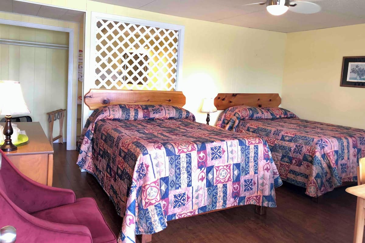 Une chambre avec deux lits, un ventilateur de plafond, une tête de lit en bois, un bureau avec une lampe et une chaise.