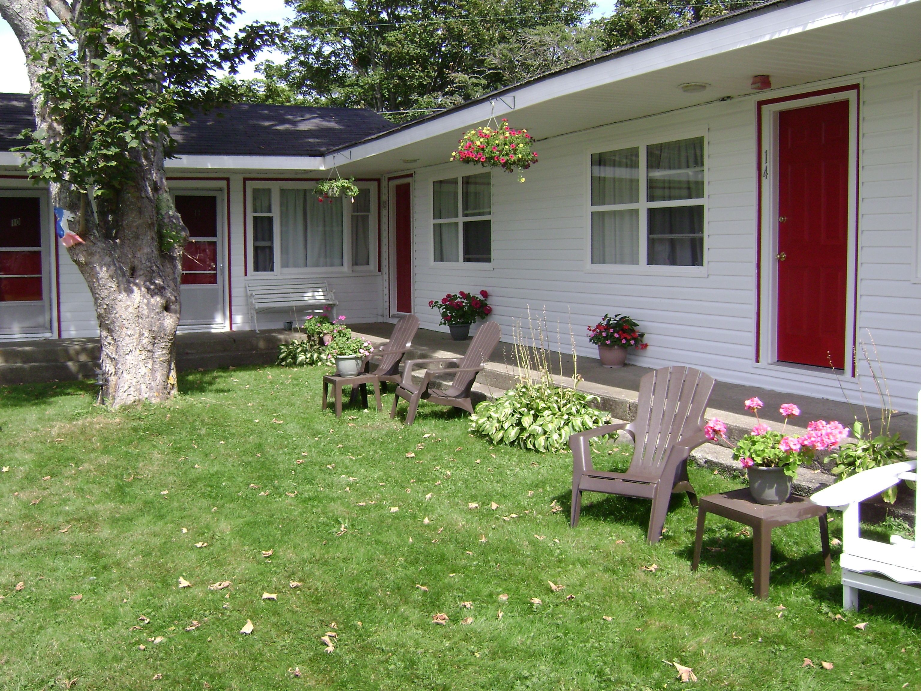 Una casa blanca con contraventanas rojas y un porche con dos sillas Adirondack.
