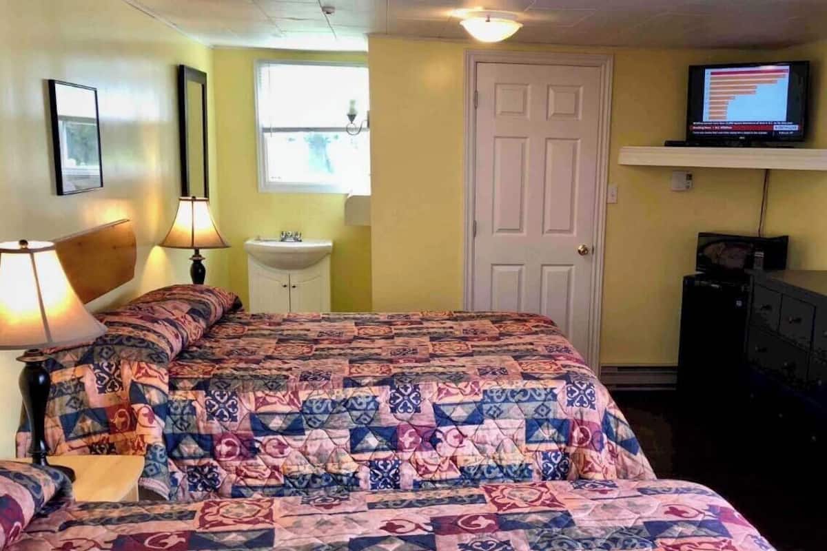 Une chambre avec un grand lit, un téléviseur posé sur une étagère et une porte.