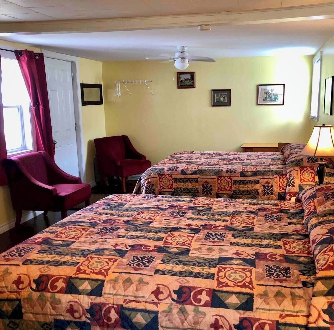 A room with two beds, a chair, a ceiling fan, and a lamp.
