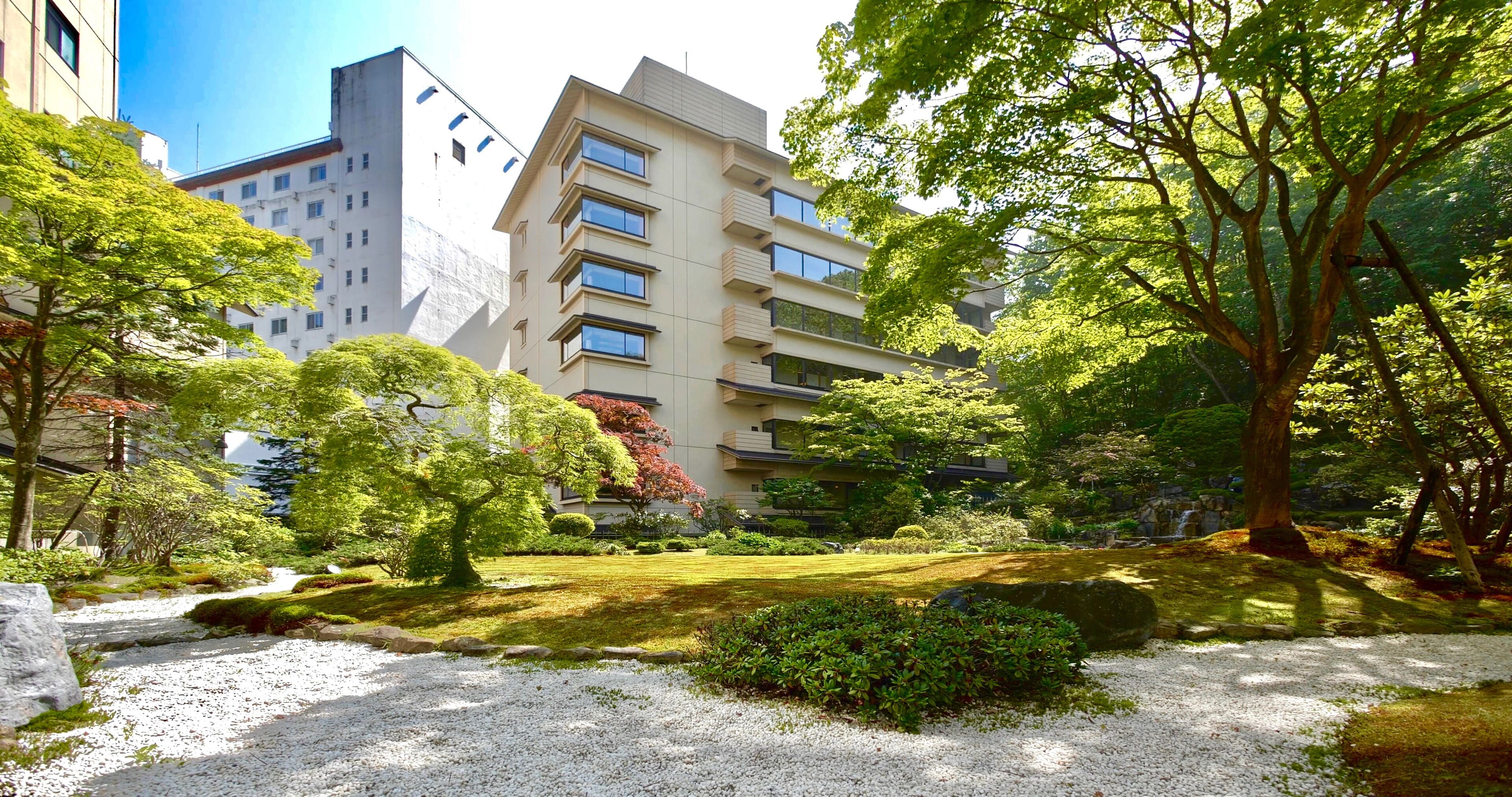 Un bâtiment moderne à plusieurs étages, doté de balcons et entouré d’une végétation luxuriante et d’un jardin bien entretenu.