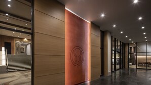 A modern interior with a wooden panel wall, a central logo, and a staircase leading to another area. - Dai-ichi Takimotokan (Noboribetsu)