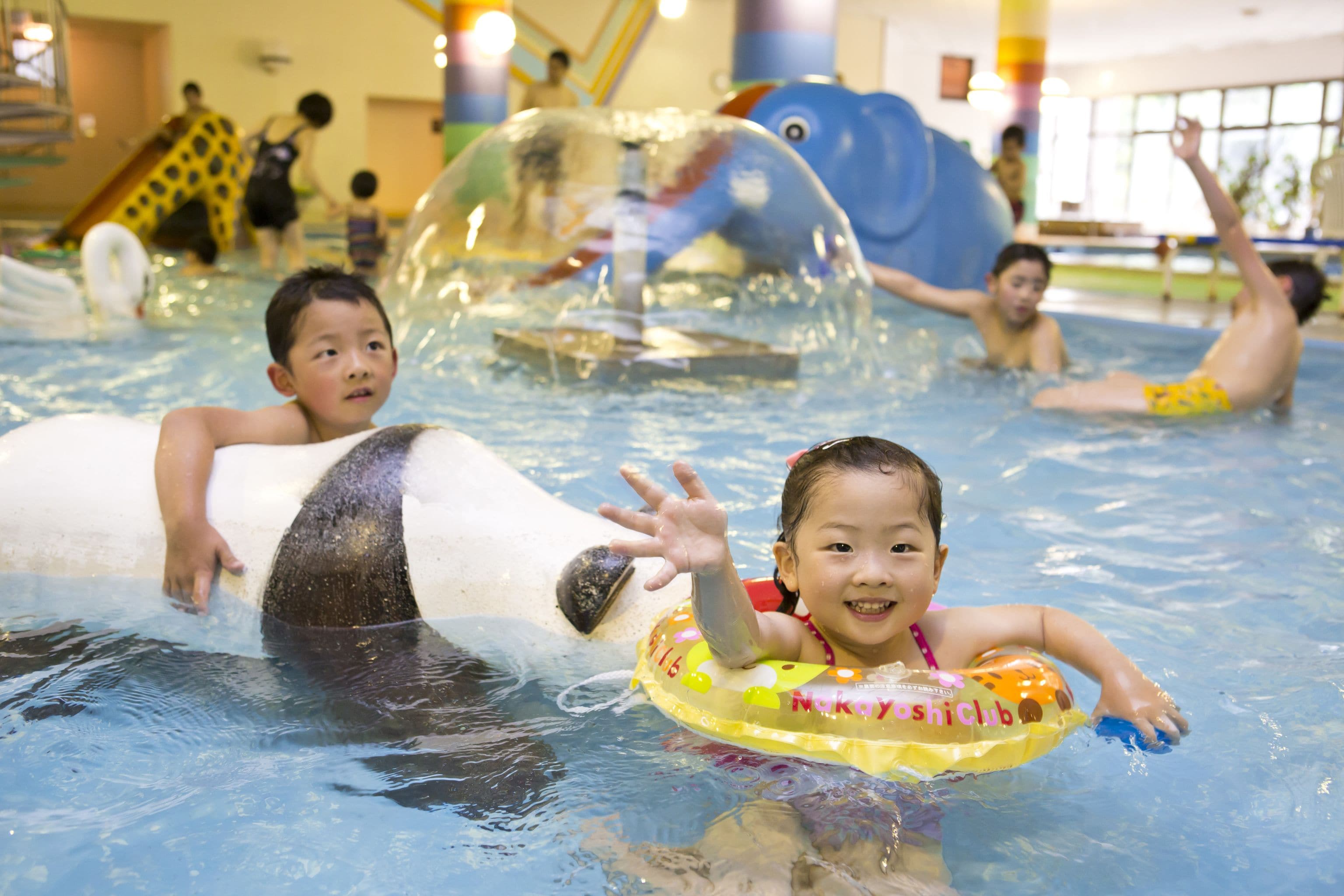 Ein Hallenbad mit verschiedenen Wasserspielelementen und aufblasbaren Spielzeugen.