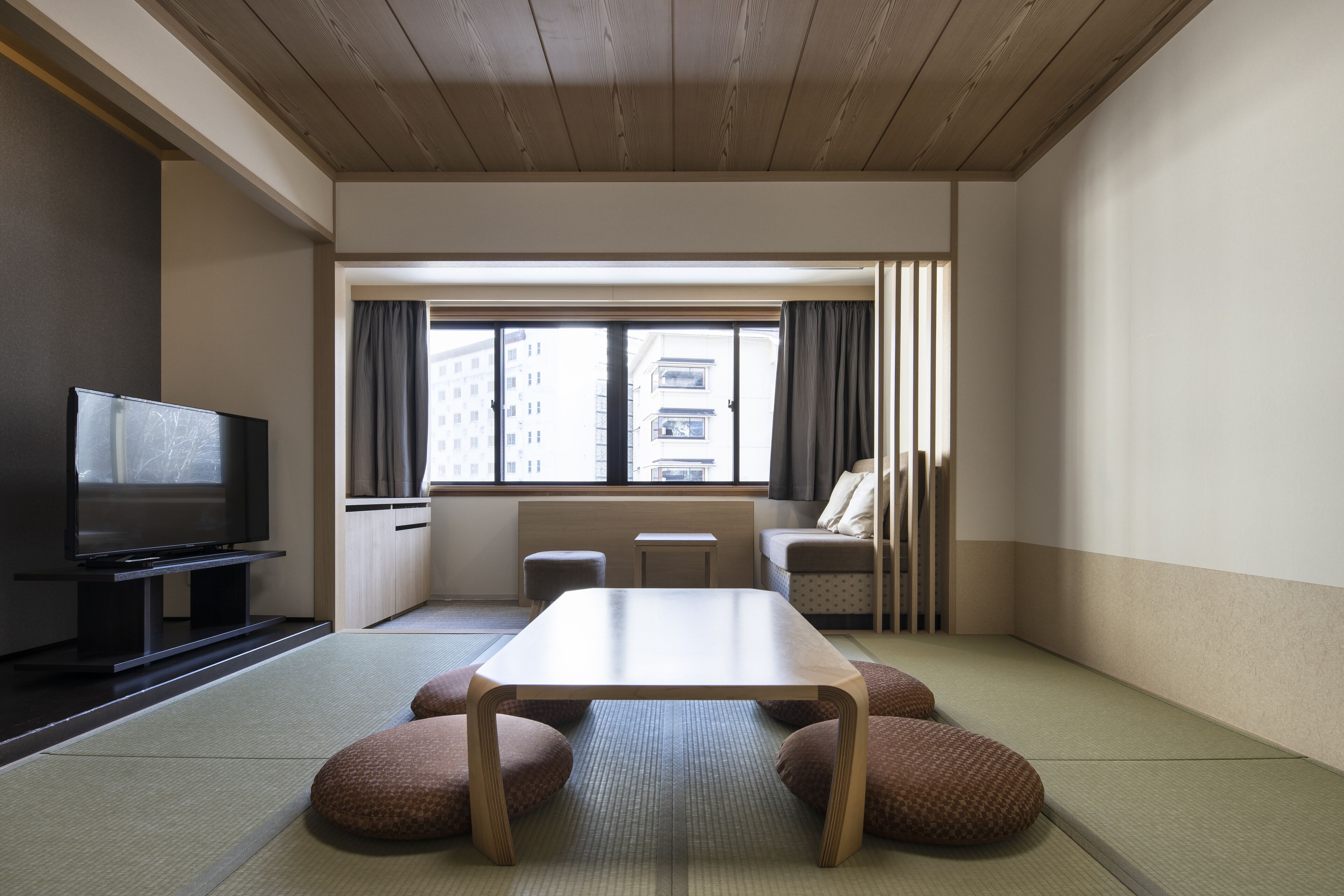 A room with tatami flooring, a television, a table, and a sofa.